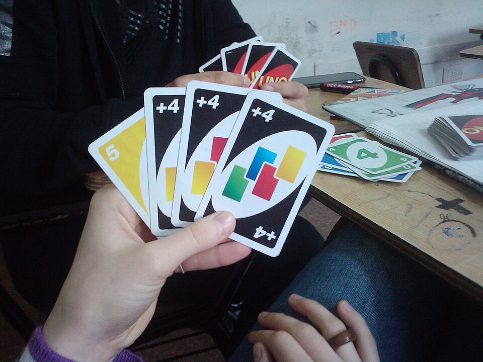 A hand holding three Wild Draw Four cards and a yellow 5 during a game of Uno
