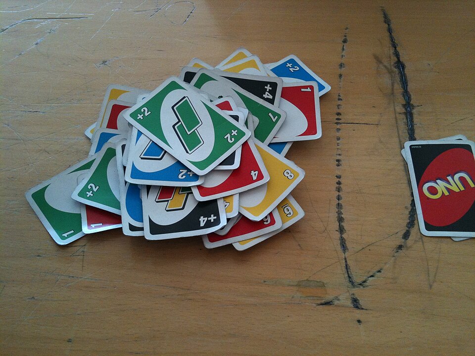 A messy pile of Uno Draw Two and Wild Draw Four cards on a wooden table